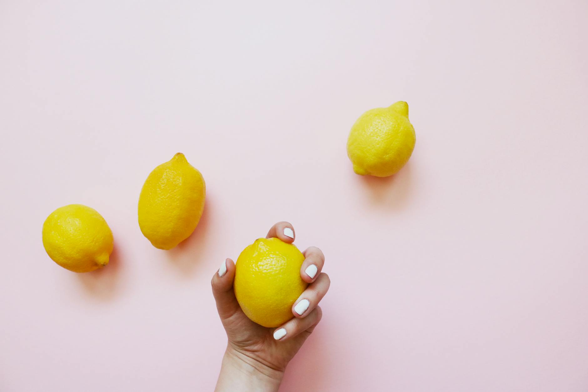 A hand holding a bright lemon against a soft pink background