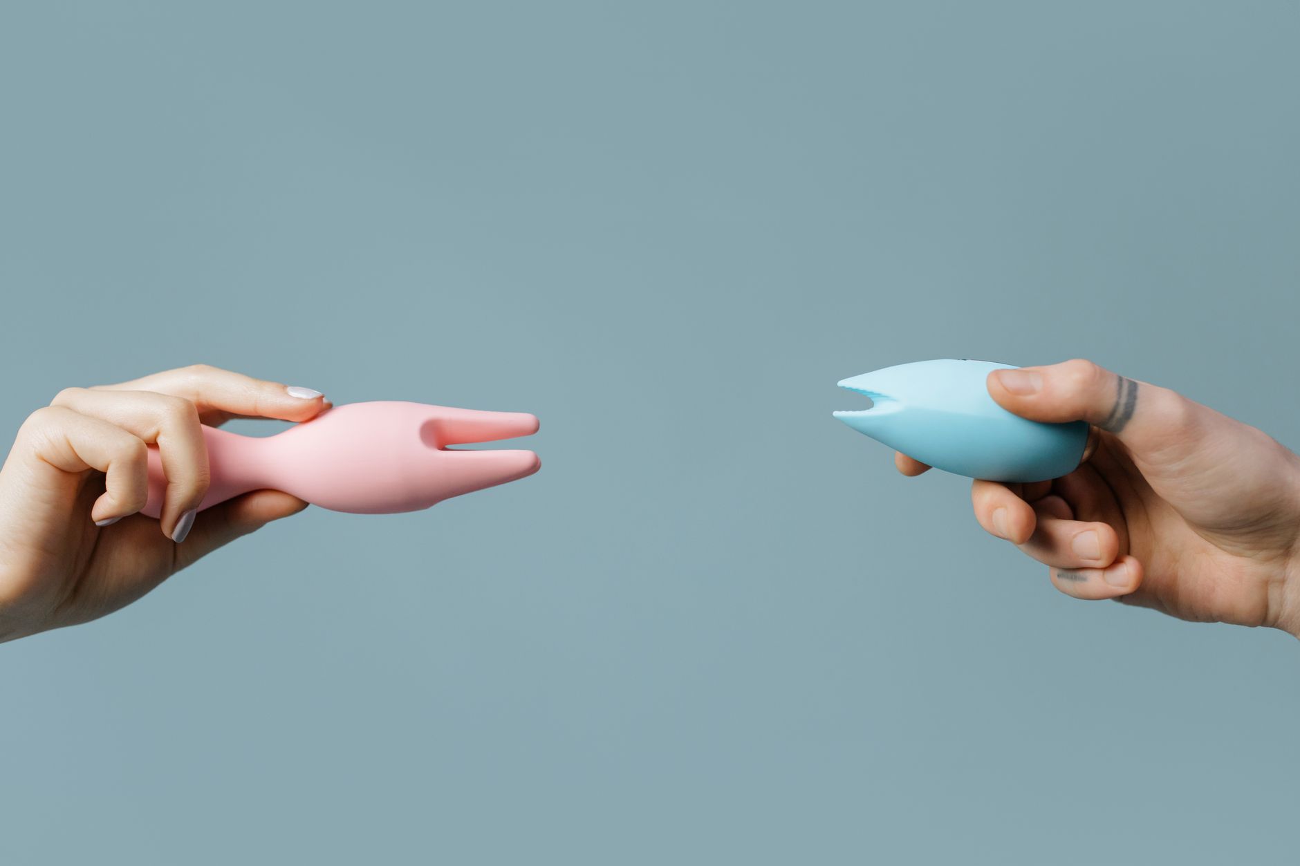 Two hands holding vibrators together against a pastel background.