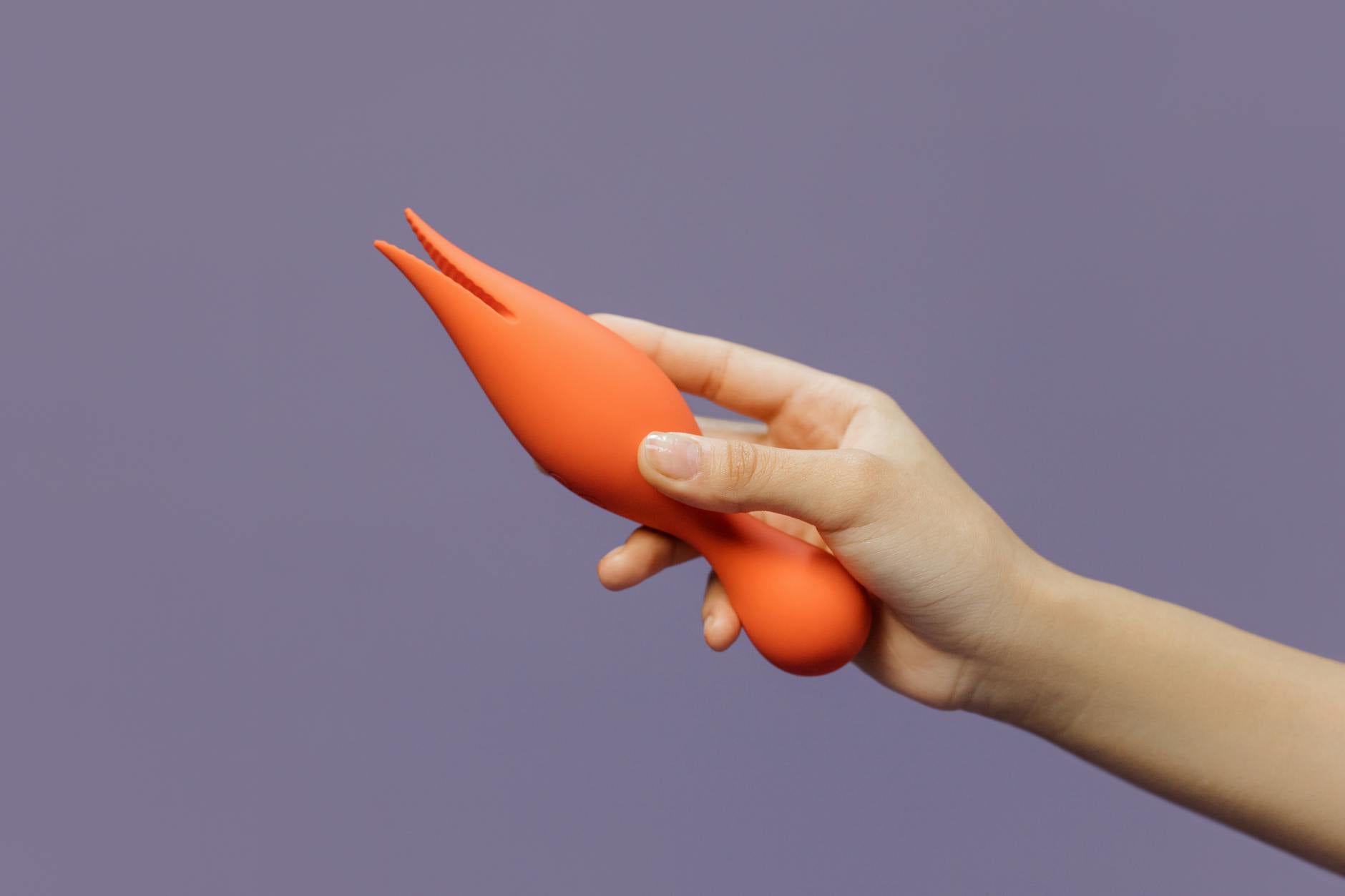 Close-up of a vibrant orange lemon vibrator held gently, symbolizing accessible pleasure on your own terms.