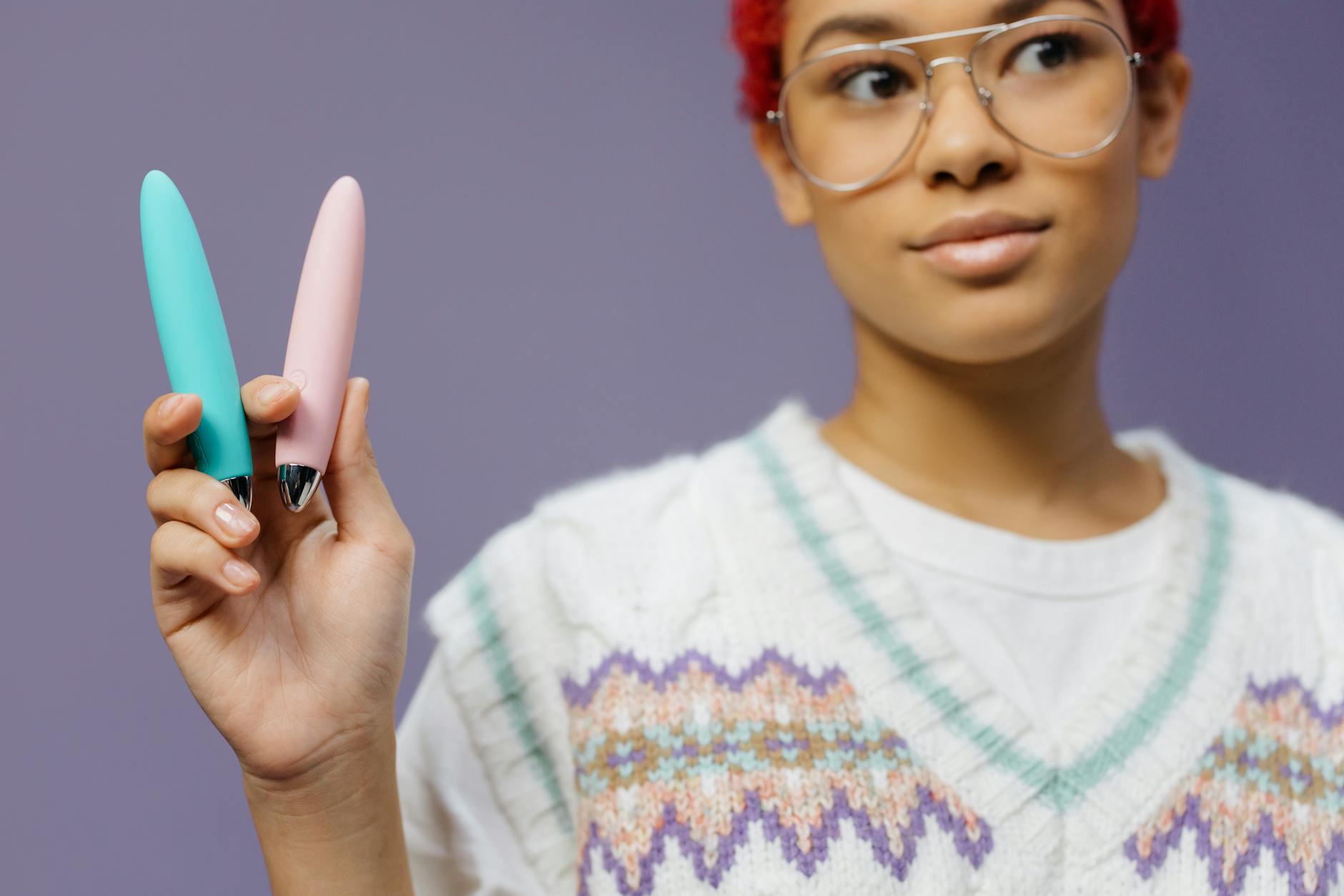 Close-up of hands holding a sleek vibrator against a purple background