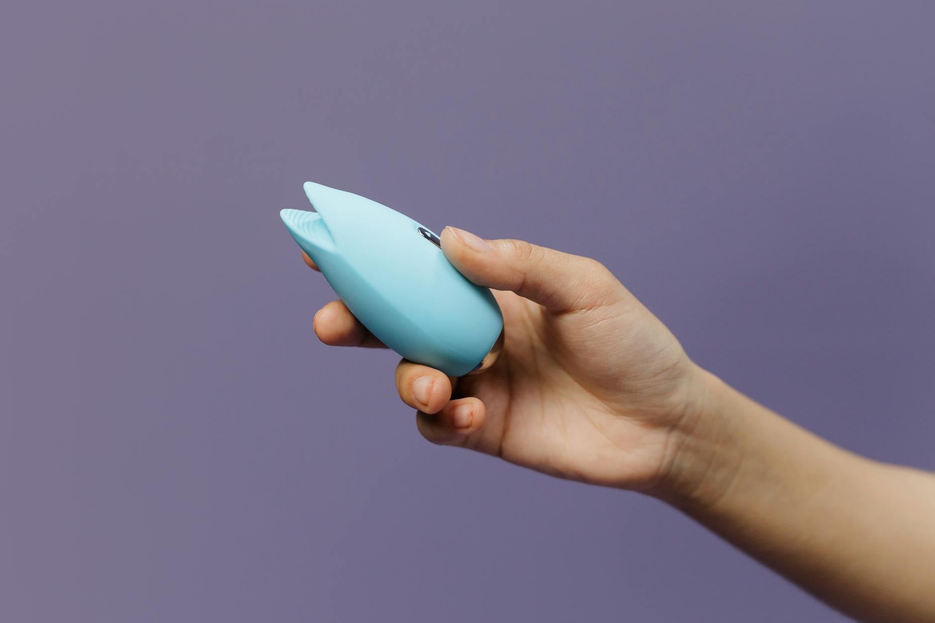 A person holding a blue silicone vibrator against a solid purple background, representing self-care and pleasure recovery