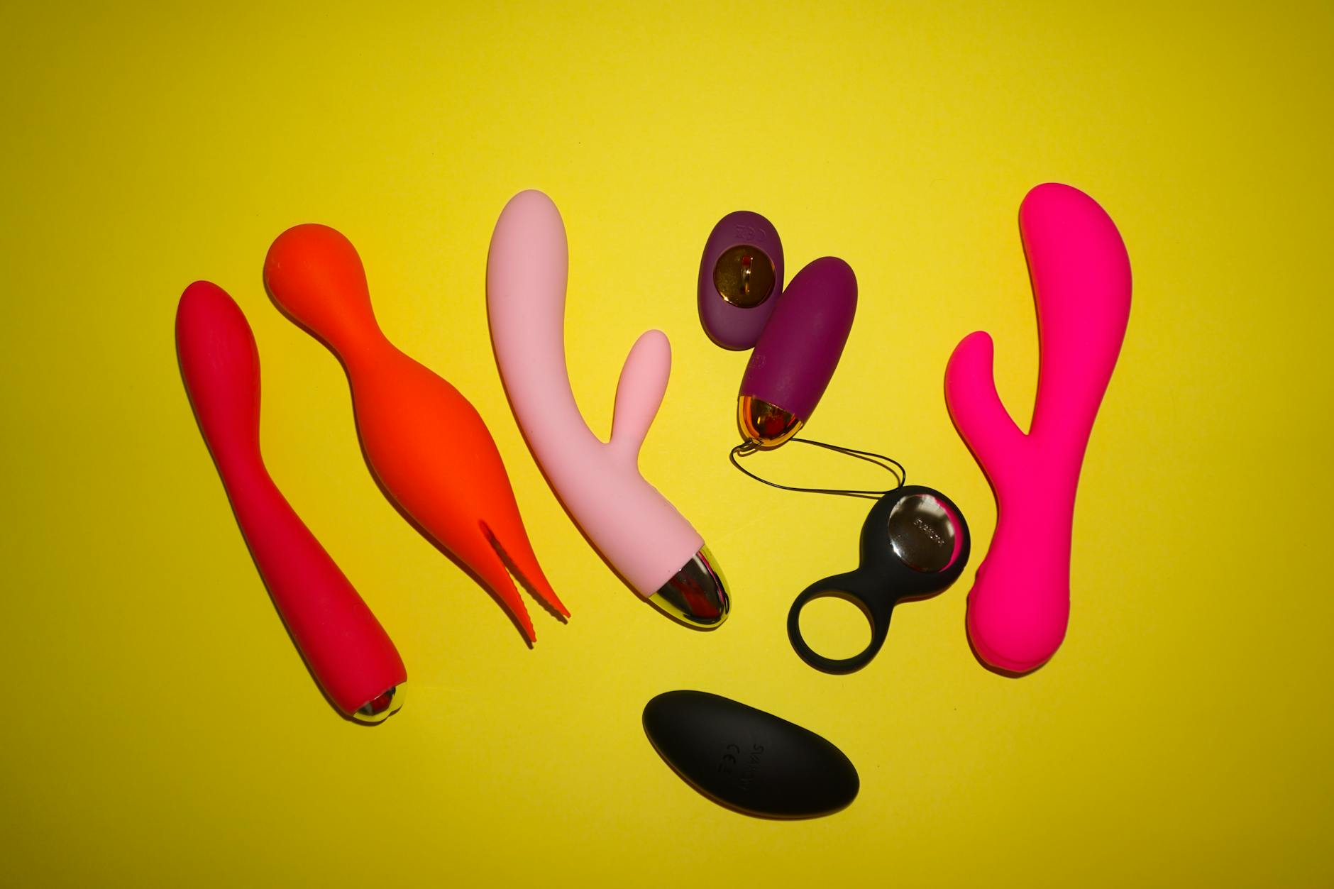 Colorful vibrators arranged on bright yellow background in studio lighting